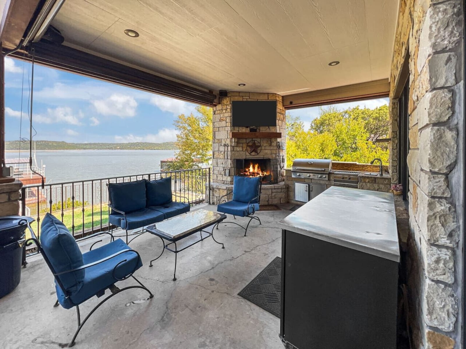 Covered lakeside patio with stone fireplace and full outdoor kitchen at PK Lake House